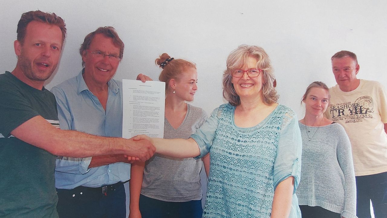 Brigitte schudt de hand van een man. Vincent houdt de statuten van Quiet omhoog. Stephanie en twee andere mensen kijken toe.