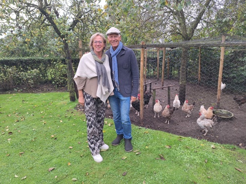 Ben en Marion staan in de tuin voor het kippenhok. Ze dragen allebei een sjaal.