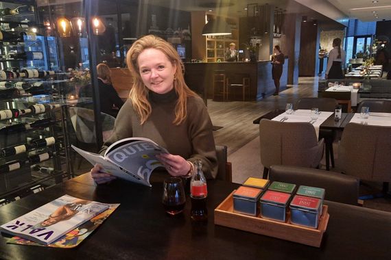 Marije zit aan een tafel in haar restaurant. Ze leest een Quiet 500.